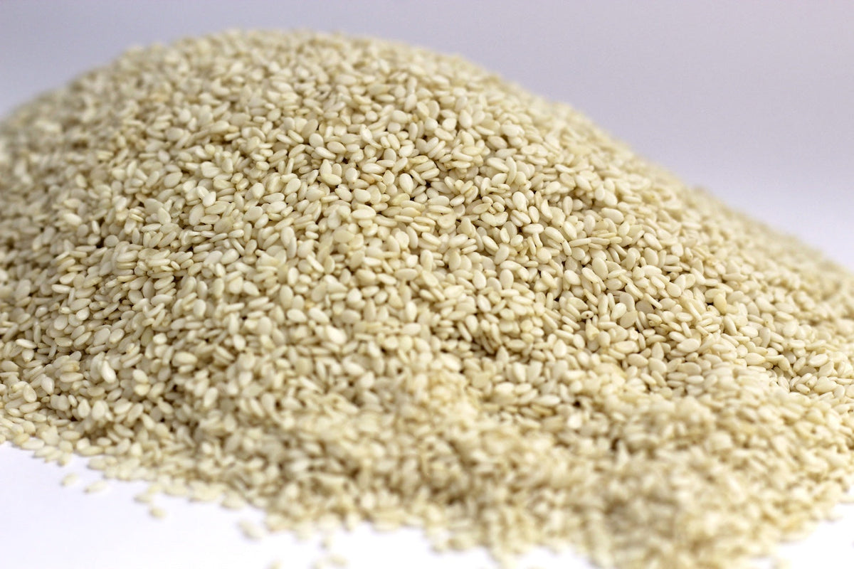 Hulled Sesame Seeds scattered in a loose heap, showing small whole ivory-colored seeds